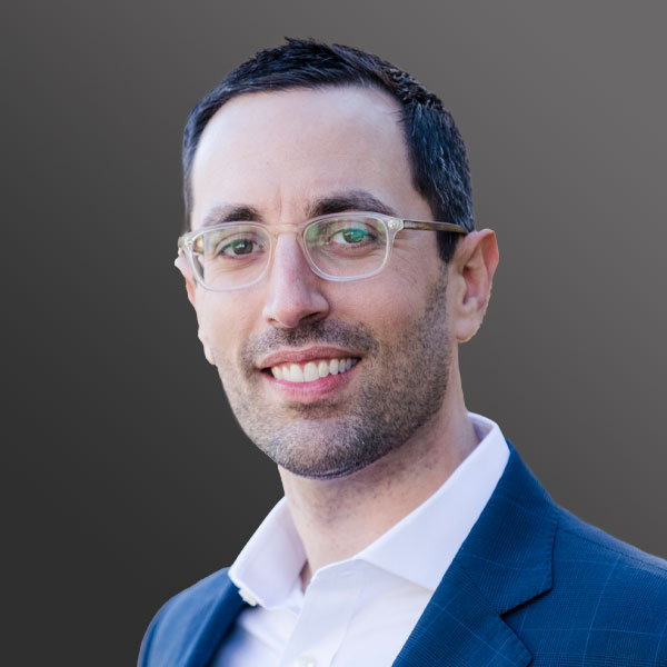 A man in glasses and a suit smiling for the camera.